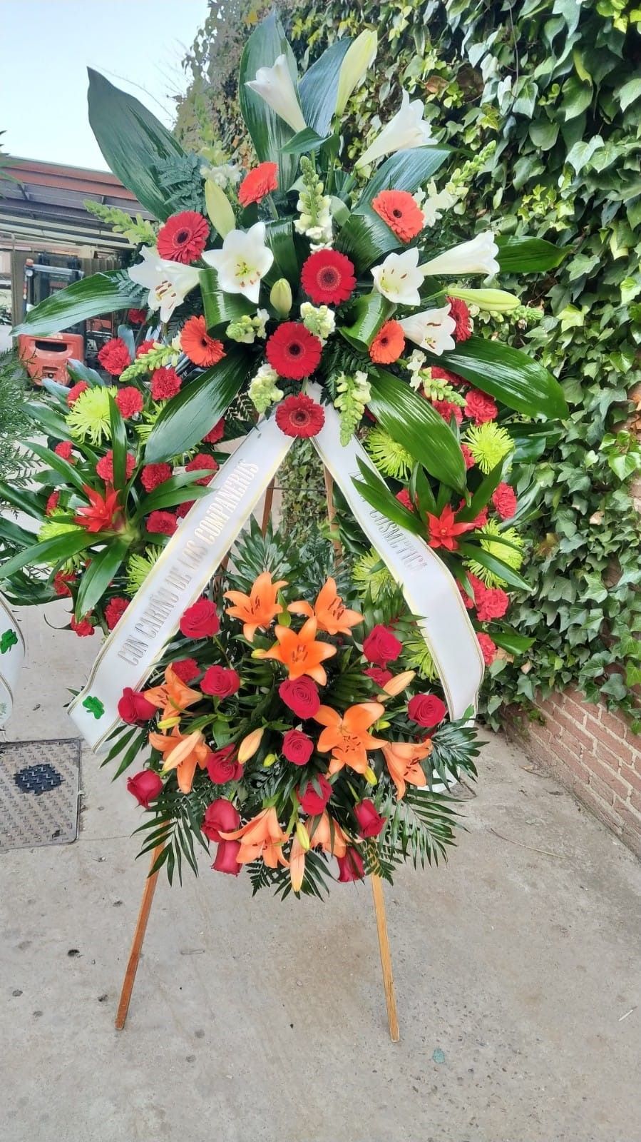 Una corona de flores con una cinta blanca está en el suelo.