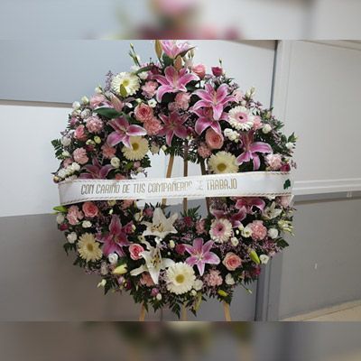 Una corona de flores rosas y blancas con una cinta que dice con cariño