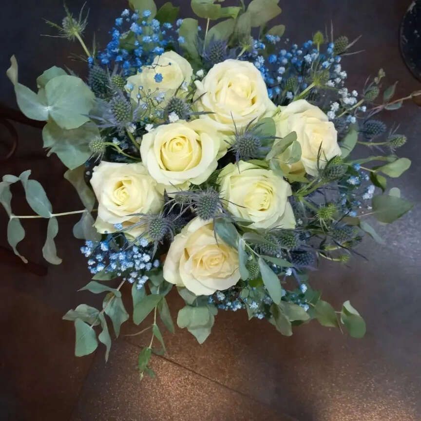 Un ramo de rosas blancas y flores azules de aliento de bebé.