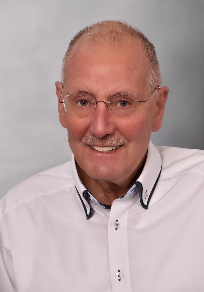 Ein Mann mit Brille und weißem Hemd lächelt in die Kamera.