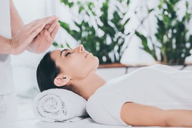 Personne allongée sur une table de massage, tandis qu’une main plane au-dessus de son front