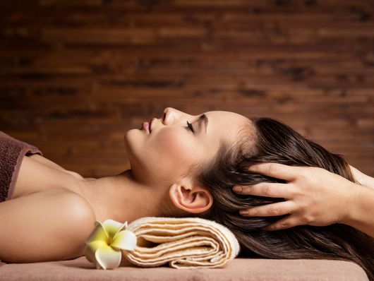 Femme recevant un massage relaxant de la tête, avec une serviette et une fleur, sur une table