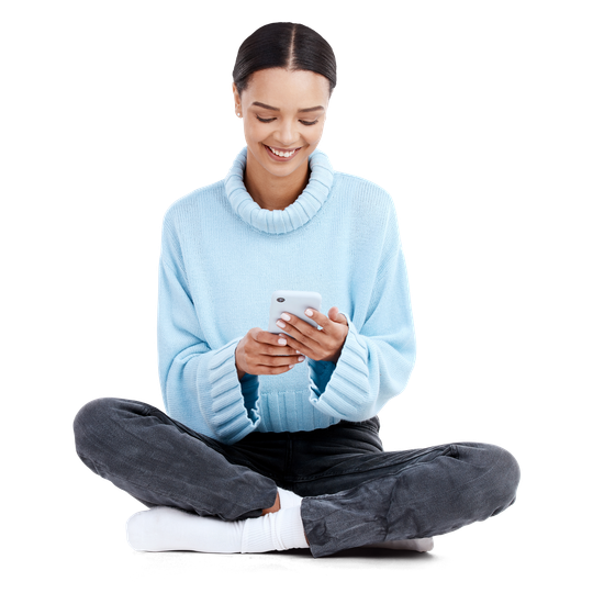 Personne souriante en pull, assise en tailleur et utilisant un Smartphone.