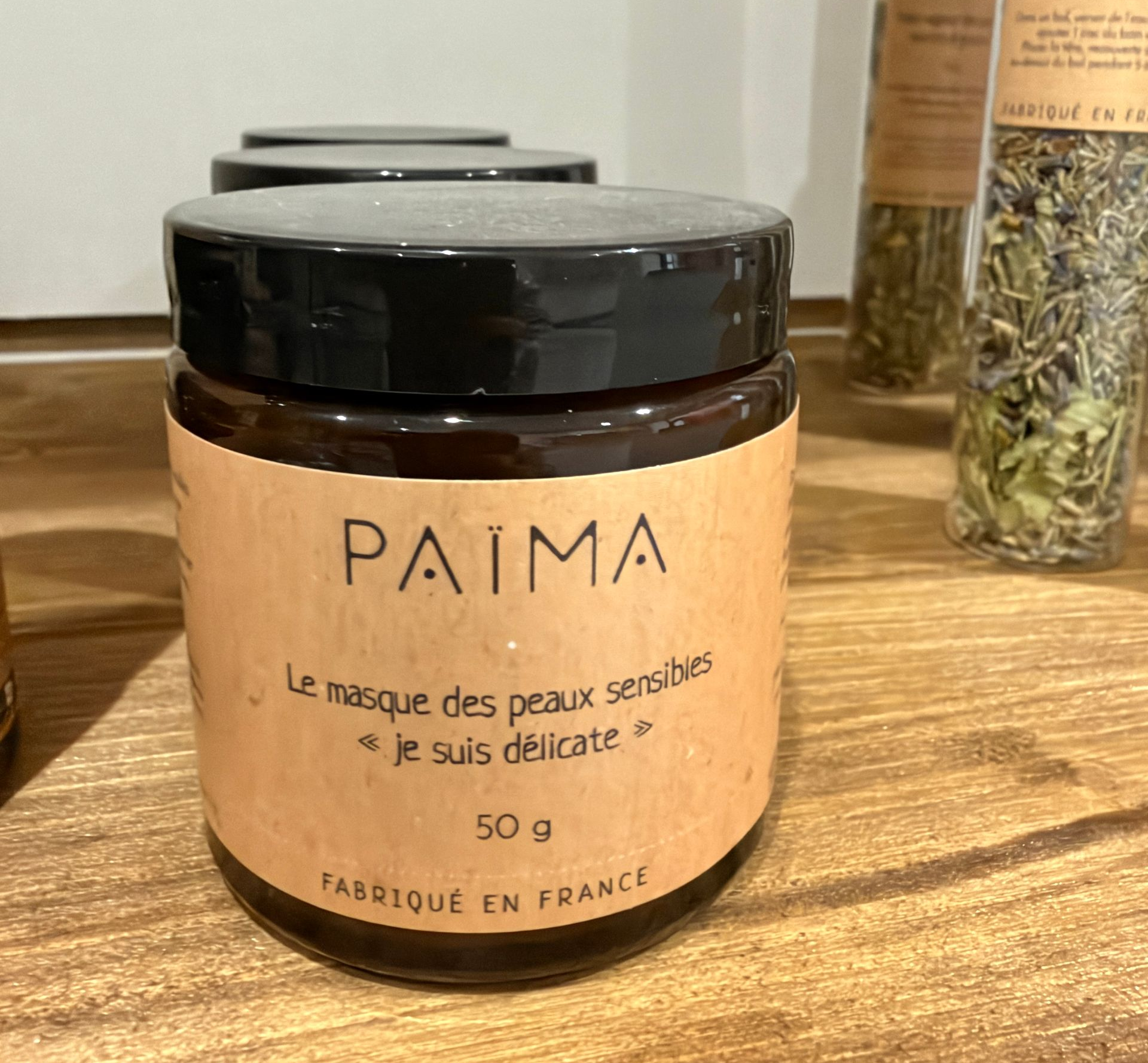 Pot de crème pour le visage PAIMA posé sur une surface, avec une étiquette en français et un couvercle.