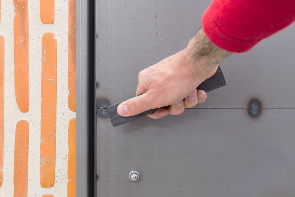Una persona sostiene una espátula sobre una pared de ladrillos.