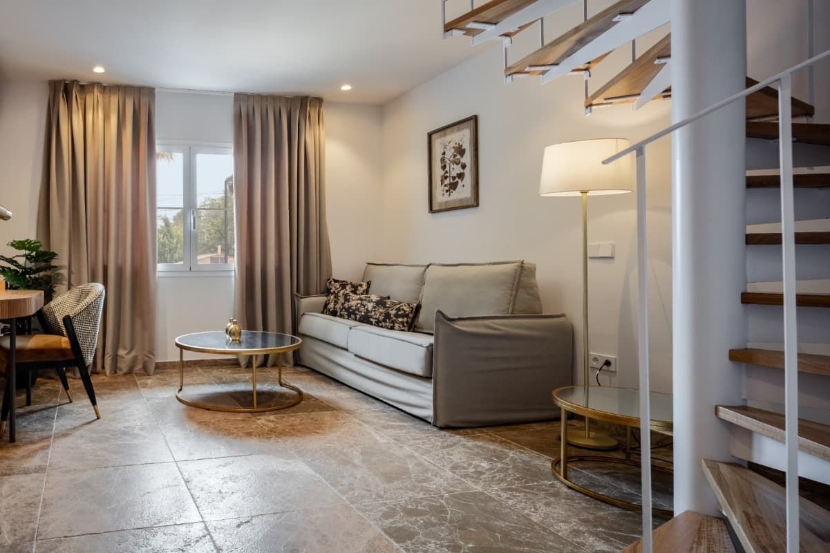 Una sala de estar con sofá, mesa, lámpara y escaleras.