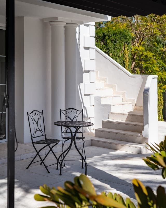 Una mesa y sillas en un porche con escaleras al fondo.