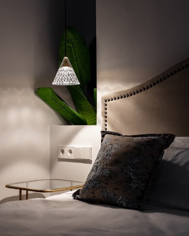 Un dormitorio con cama, mesita de noche, lámpara y planta.