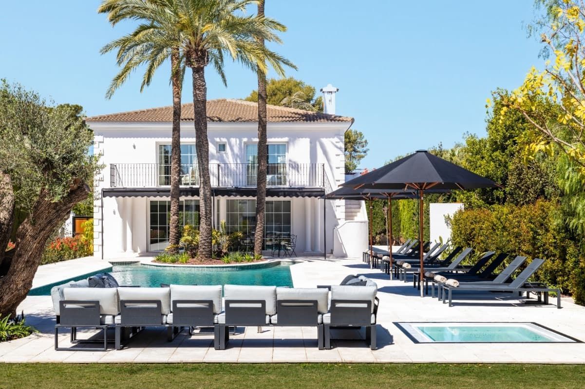 Una gran casa blanca con una piscina y sillas delante de ella.