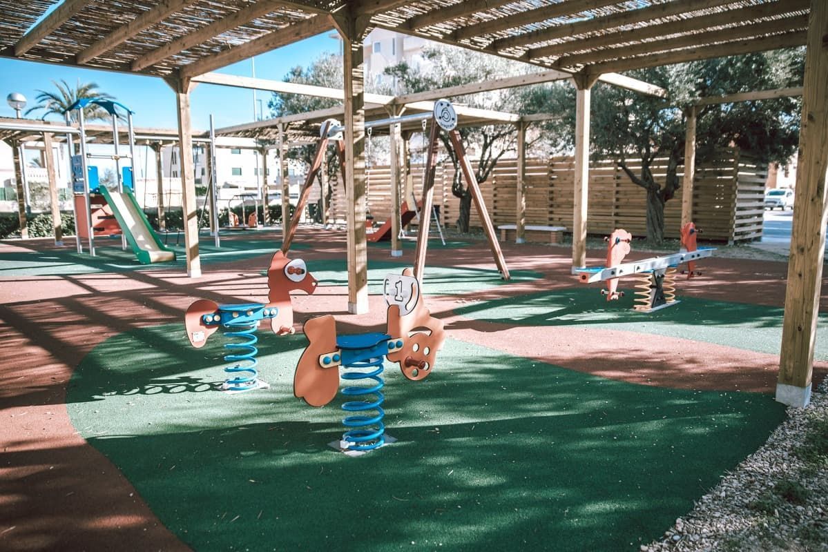 Un parque infantil con columpios y un tobogán bajo un dosel.