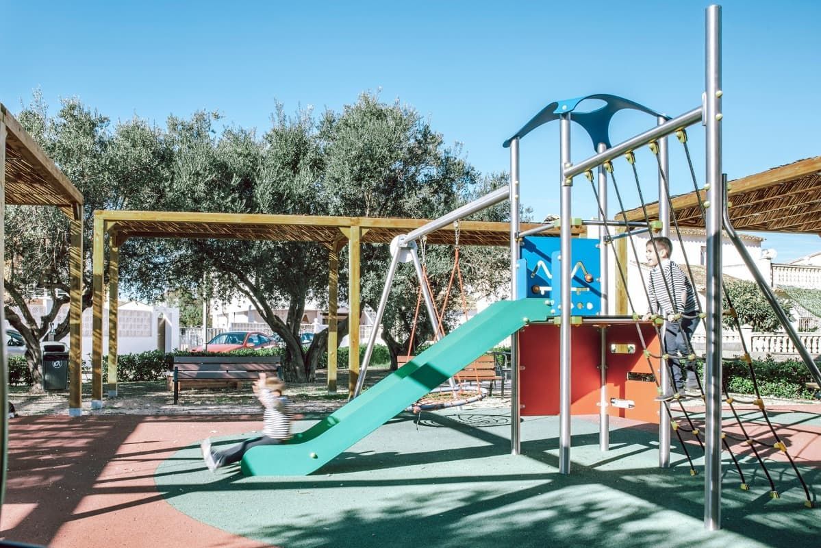 Un niño está jugando en un parque infantil con un tobogán y columpios.