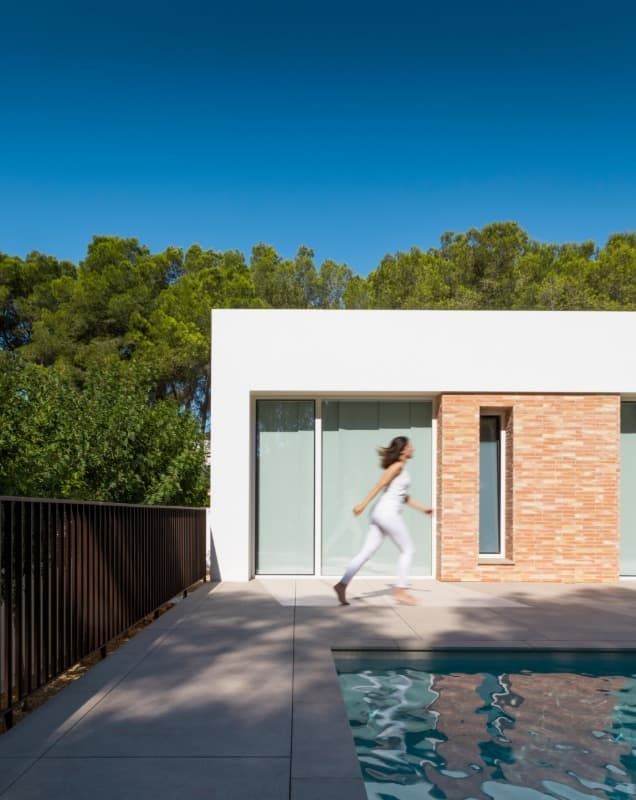 Una mujer corre frente a una casa al lado de una piscina.
