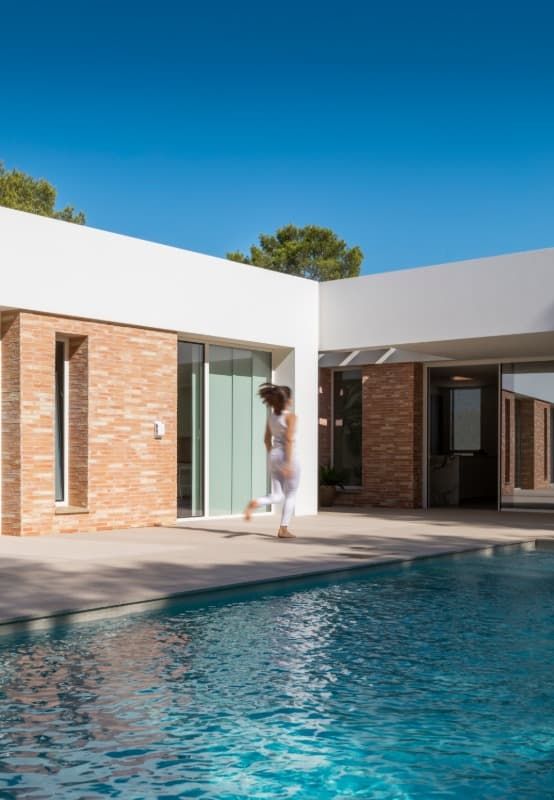 Una mujer camina por una piscina frente a una casa.