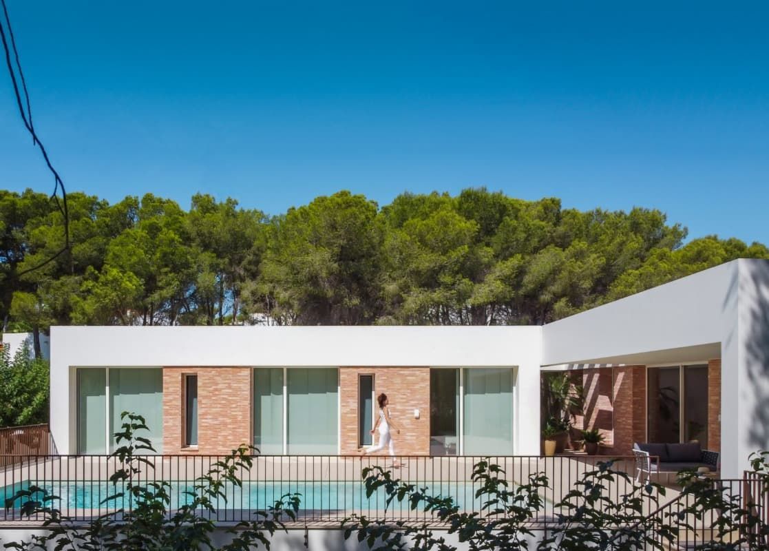 Un hombre camina frente a una casa moderna con piscina.
