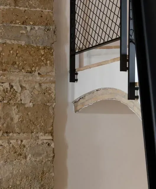 Una escalera con barandilla de metal está al lado de un muro de piedra.