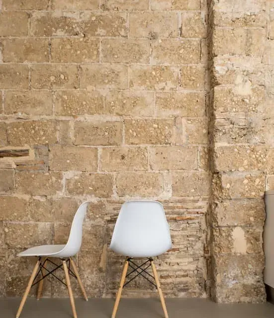 Dos sillas blancas están sentadas frente a una pared de ladrillos.