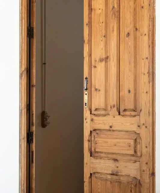 Una puerta de madera se abre a una habitación con una pared blanca.