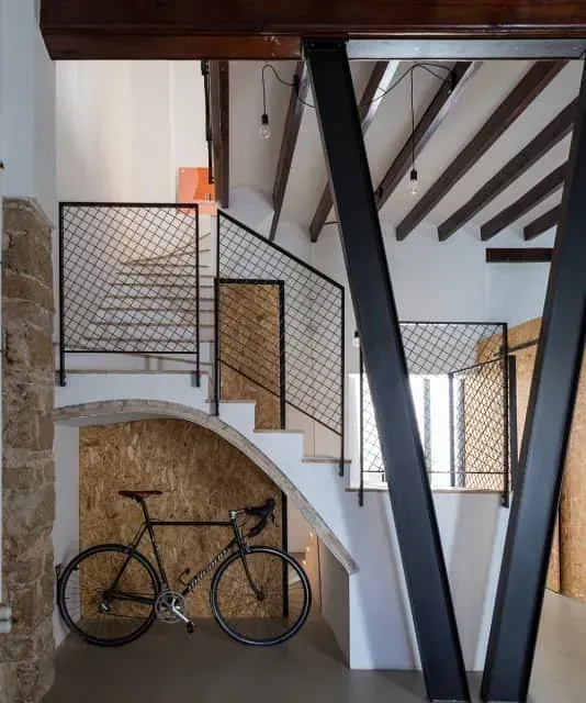 Una bicicleta está estacionada debajo de una escalera en una casa.