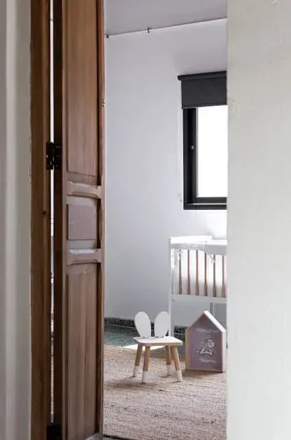 Una puerta de madera se abre a una habitación con una cuna y una silla.