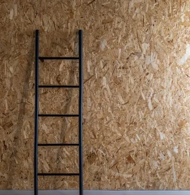 Una escalera negra está apoyada contra una pared de madera.