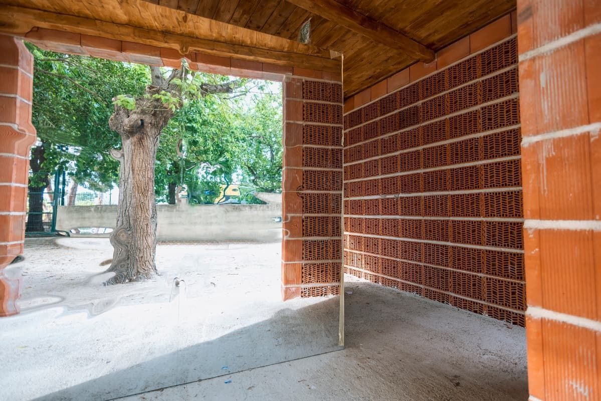 Una pared de ladrillos con techo de madera y un árbol al fondo.