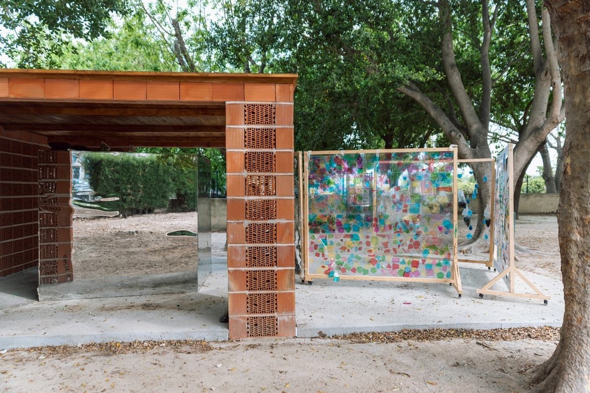 Una pared de ladrillos con grafitis en un parque al lado de un árbol.