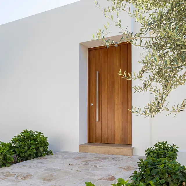 Un edificio blanco con una puerta de madera y un árbol delante.