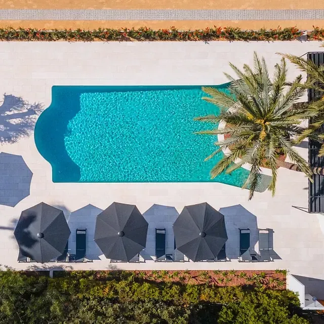 Una vista aérea de una piscina rodeada de sombrillas y palmeras.