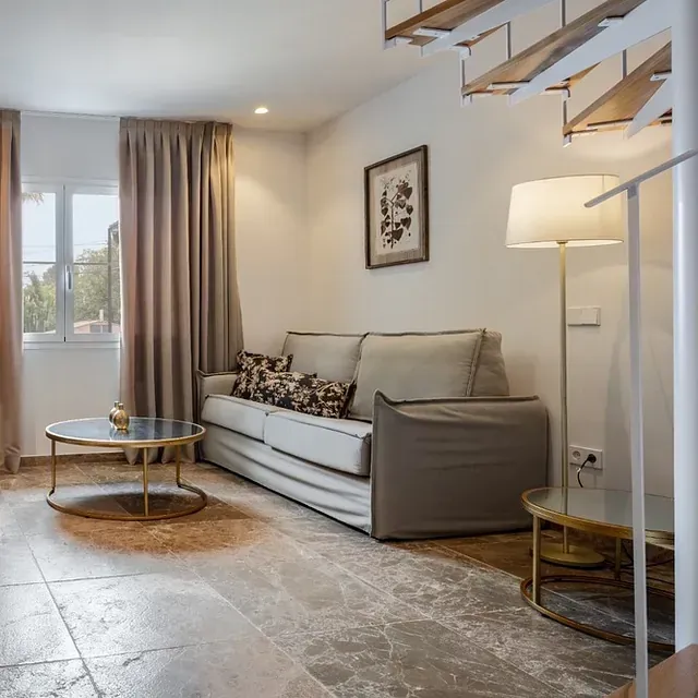 Una sala de estar con sofá, mesa de café, lámpara y escaleras.