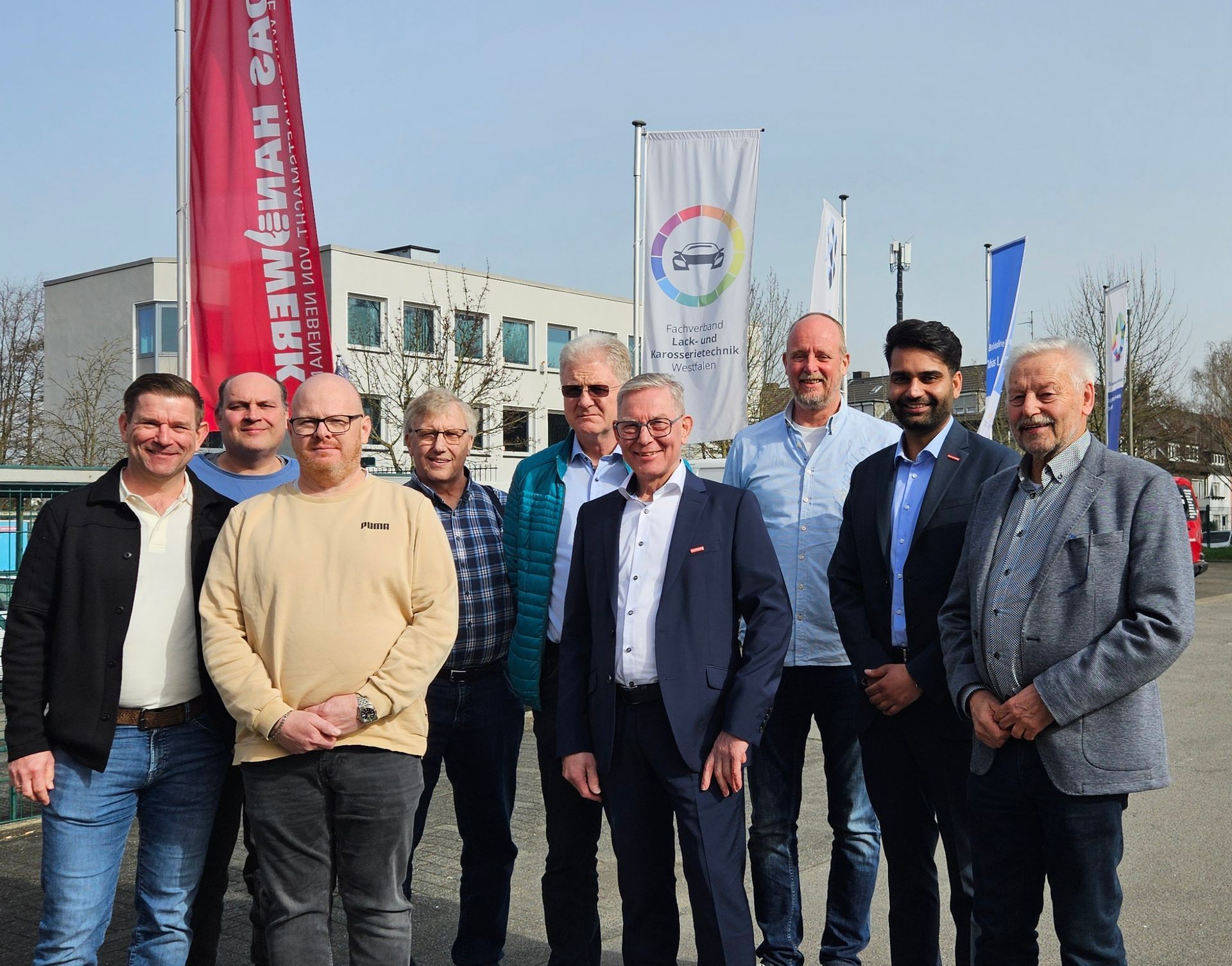 Acht Personen posieren an einem sonnigen Tag im Freien vor Bannern und Flaggen.