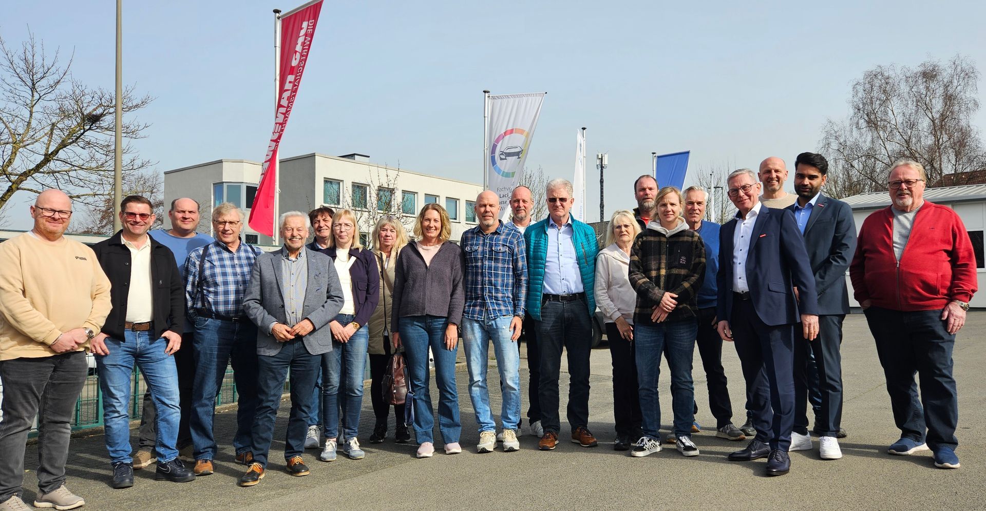 Eine Gruppe von Menschen steht an einem sonnigen Tag im Freien vor einem Gebäude und posiert gemeinsam.