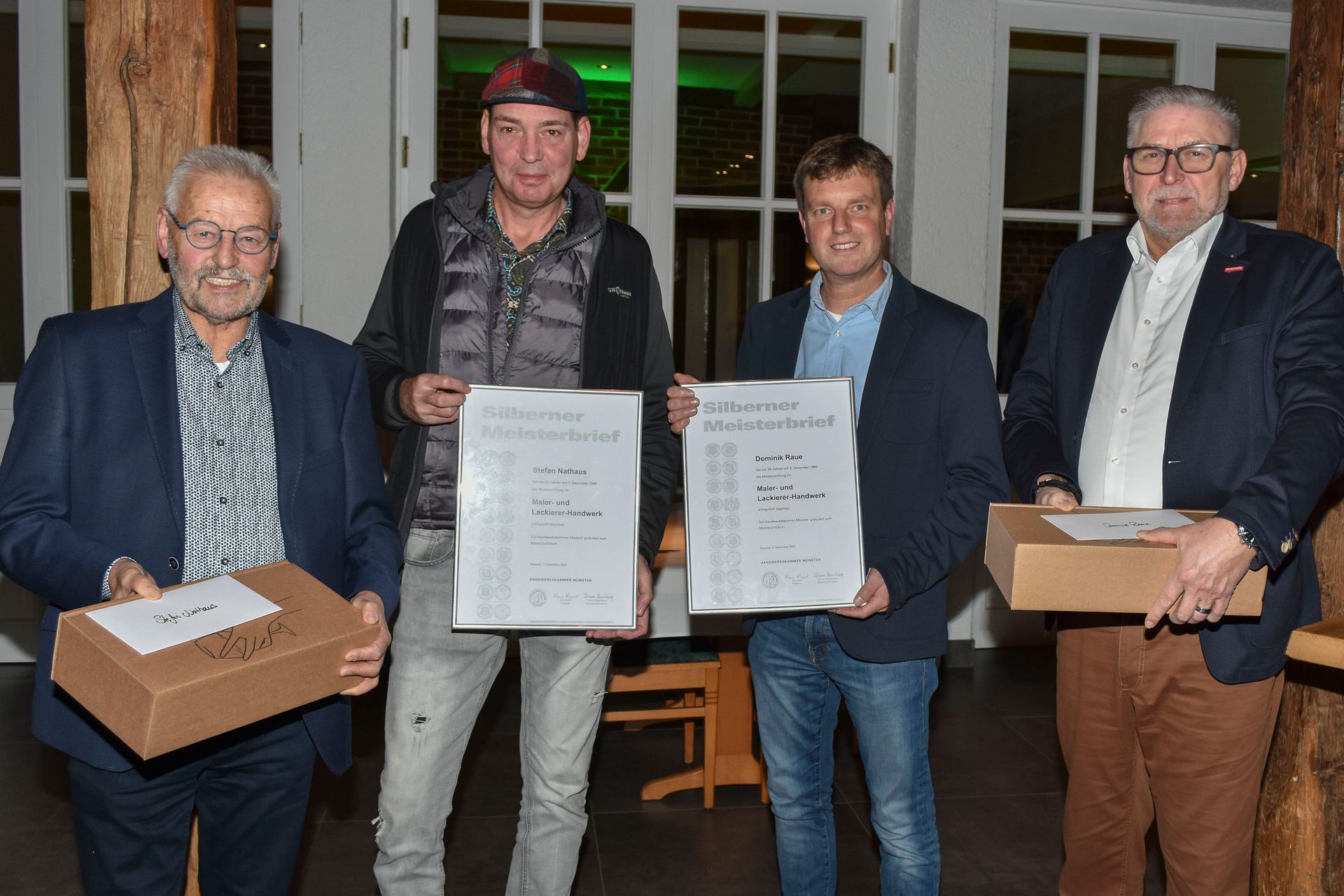 Vier Männer stehen bei einer Preisverleihung in einem Innenraum und halten Plaketten und Schachteln in den Händen.