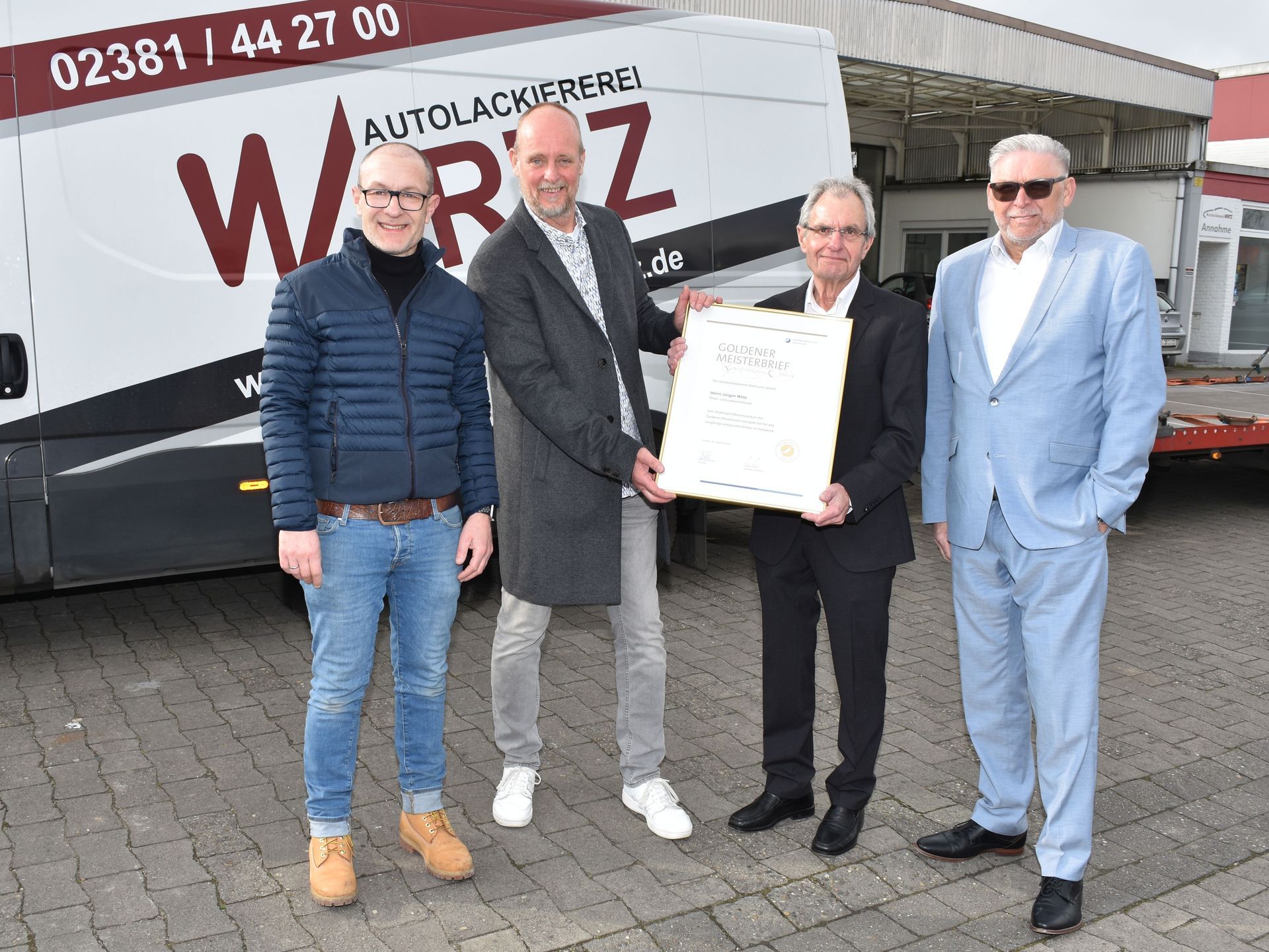 Vier Männer stehen im Freien vor einem Reisebus und halten eine gerahmte Urkunde in die Höhe.