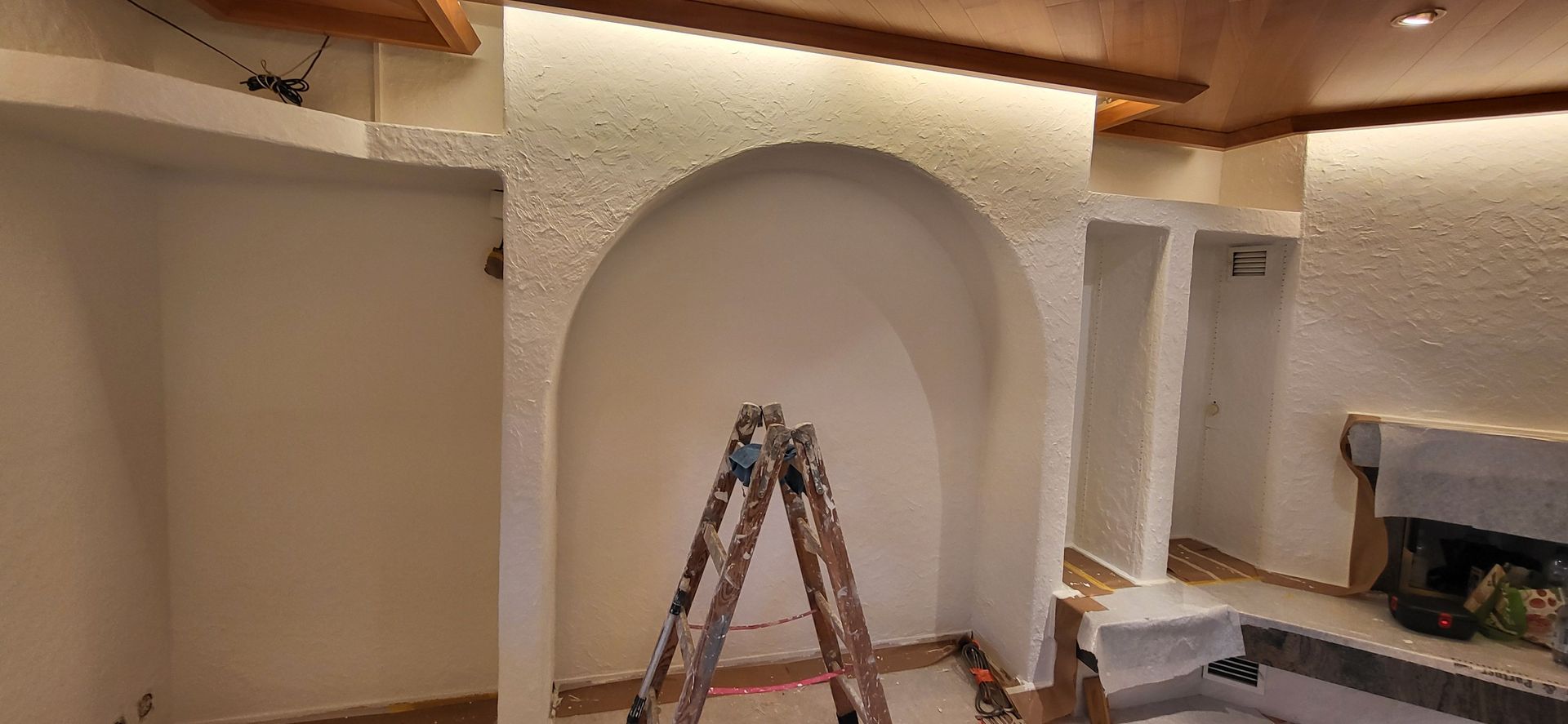 Innenraum mit gewölbter Wandnische, Holzbalken an der Decke und einer Leiter.