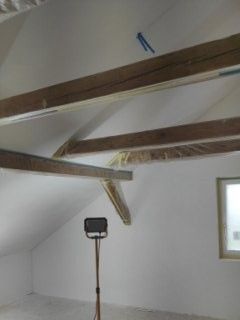 Innenansicht eines Dachbodens mit freiliegenden Holzbalken, weissen Wänden und einer Arbeitsleuchte.