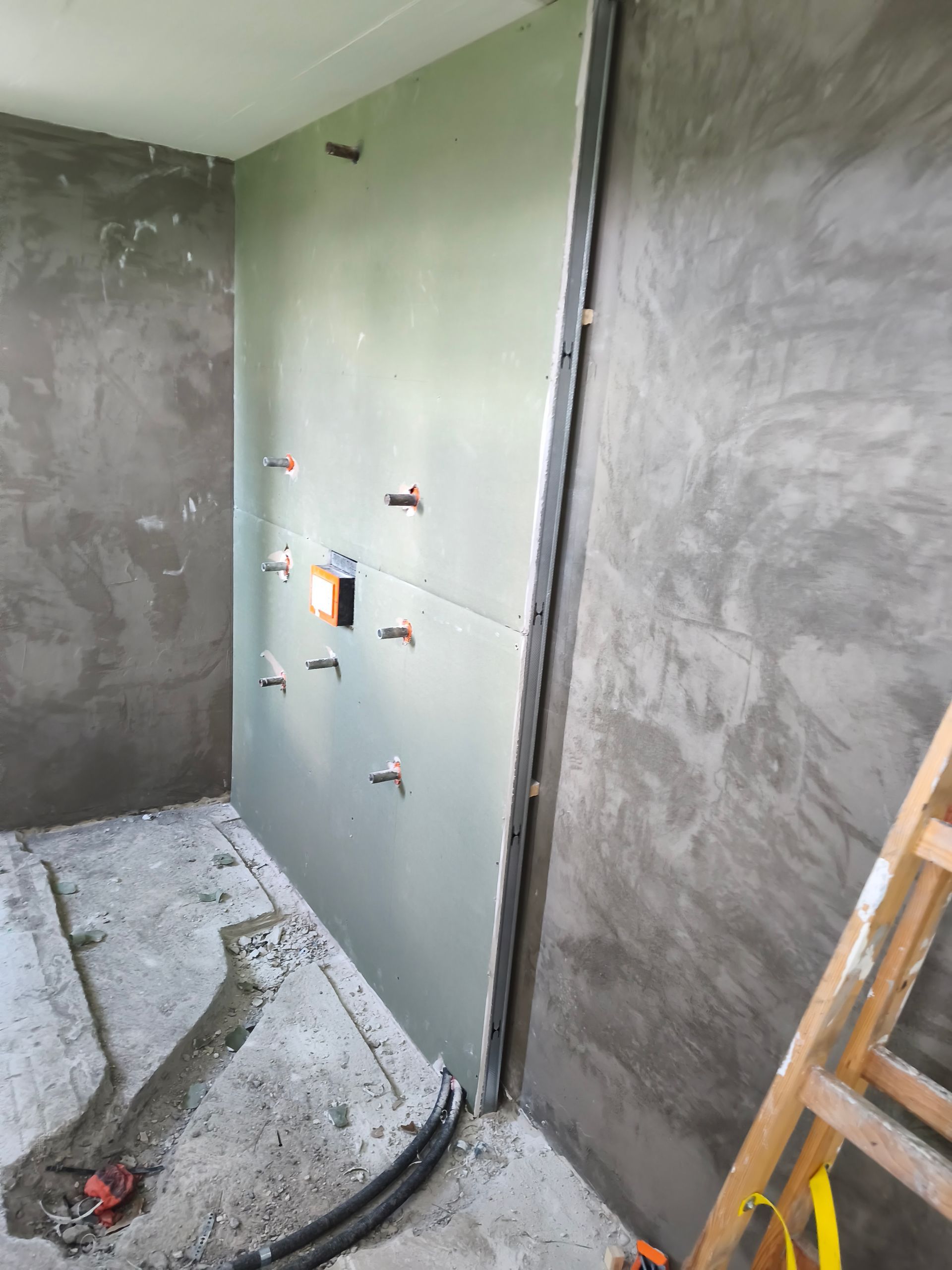 Das Badezimmer befindet sich im Bau, die Wände sind mit Gipskartonplatten verkleidet und mit Sanitär- und Elektroinstallationen versehen. Graue Wände, unfertiger Boden.