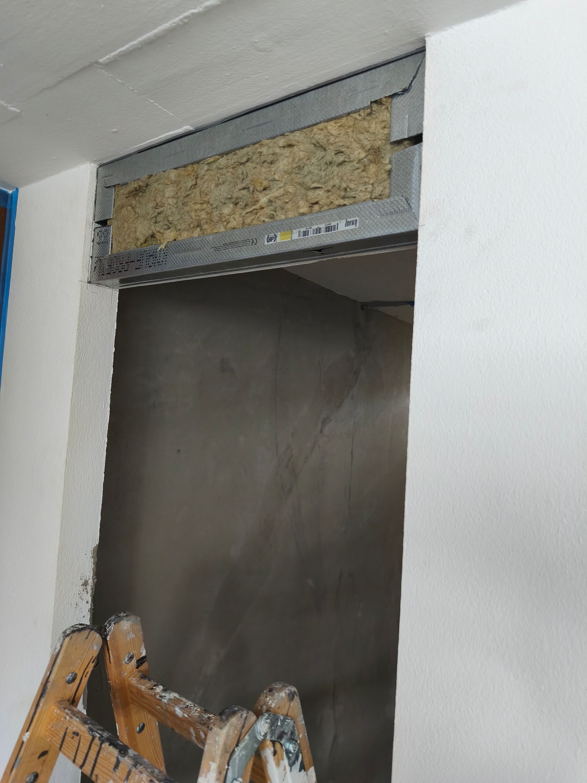 Offener Türrahmen mit Isolierung und Metallstützen; Leiter im Vordergrund.