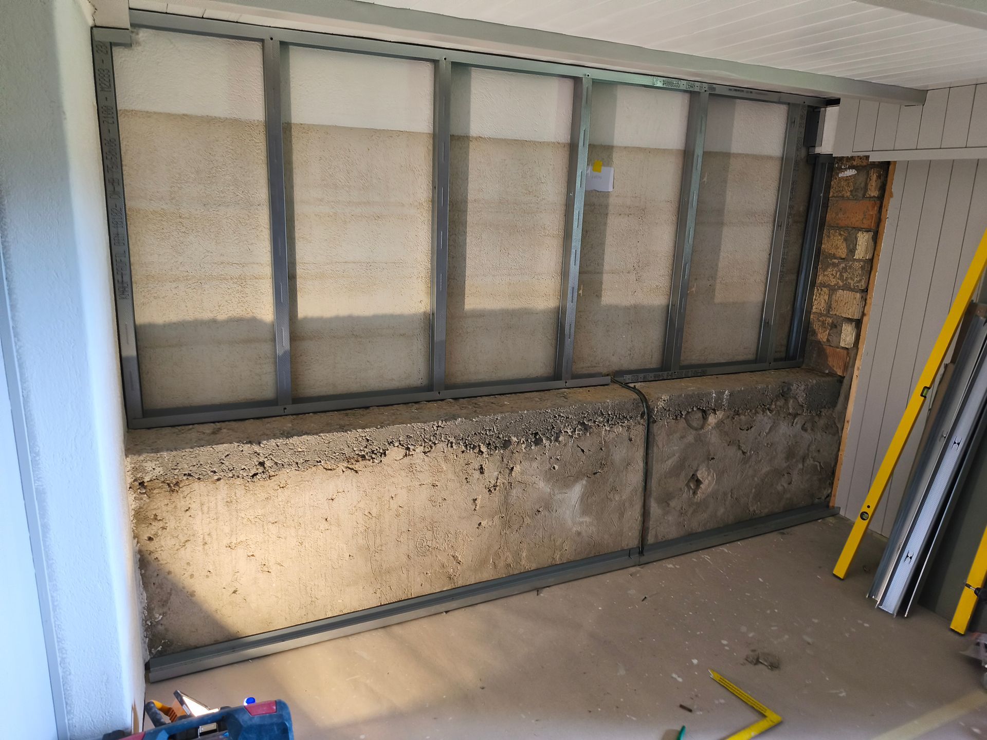 Baustelle: Metallrahmen mit Betonblöcken am Sockel, darüber Dämmung und rechts eine Ziegelmauer.