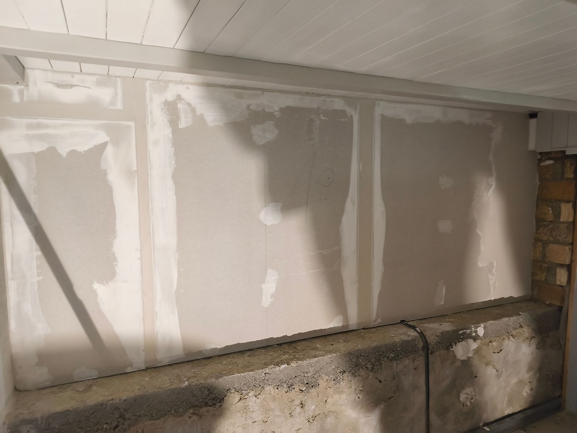 Wand mit Gipskartonstellen; teilweise fertiggestellt, hellgrau mit weisser Fugenmasse; Betonsockel.