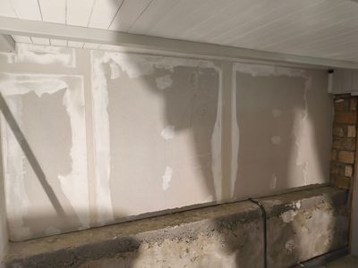 Wand mit Gipskartonstellen; teilweise fertiggestellt, hellgrau mit weisser Fugenmasse; Betonsockel.