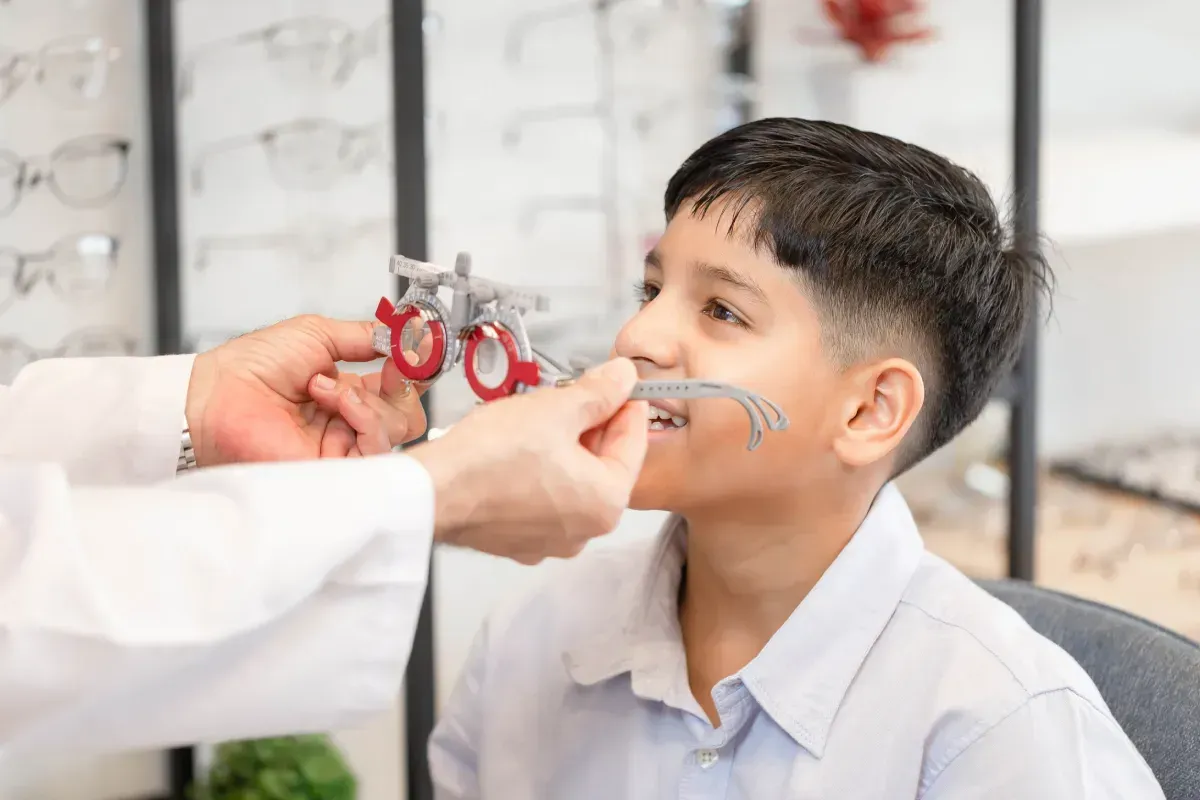 Un niño se hace un examen de la vista en el consultorio de un optometrista, mientras un médico ajusta los lentes de prueba.