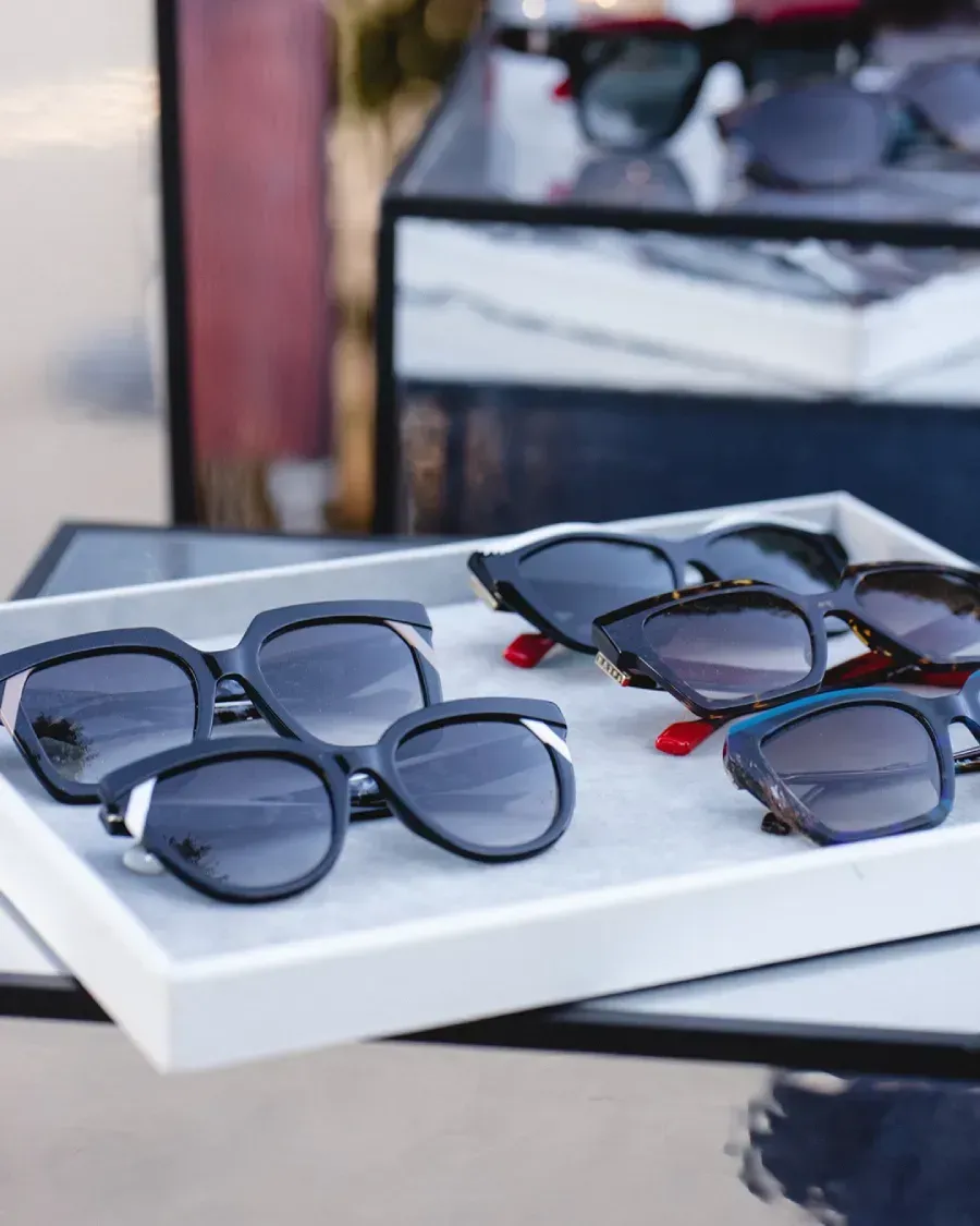 Gafas de sol expuestas en bandeja con superficie espejada; varios estilos y colores.