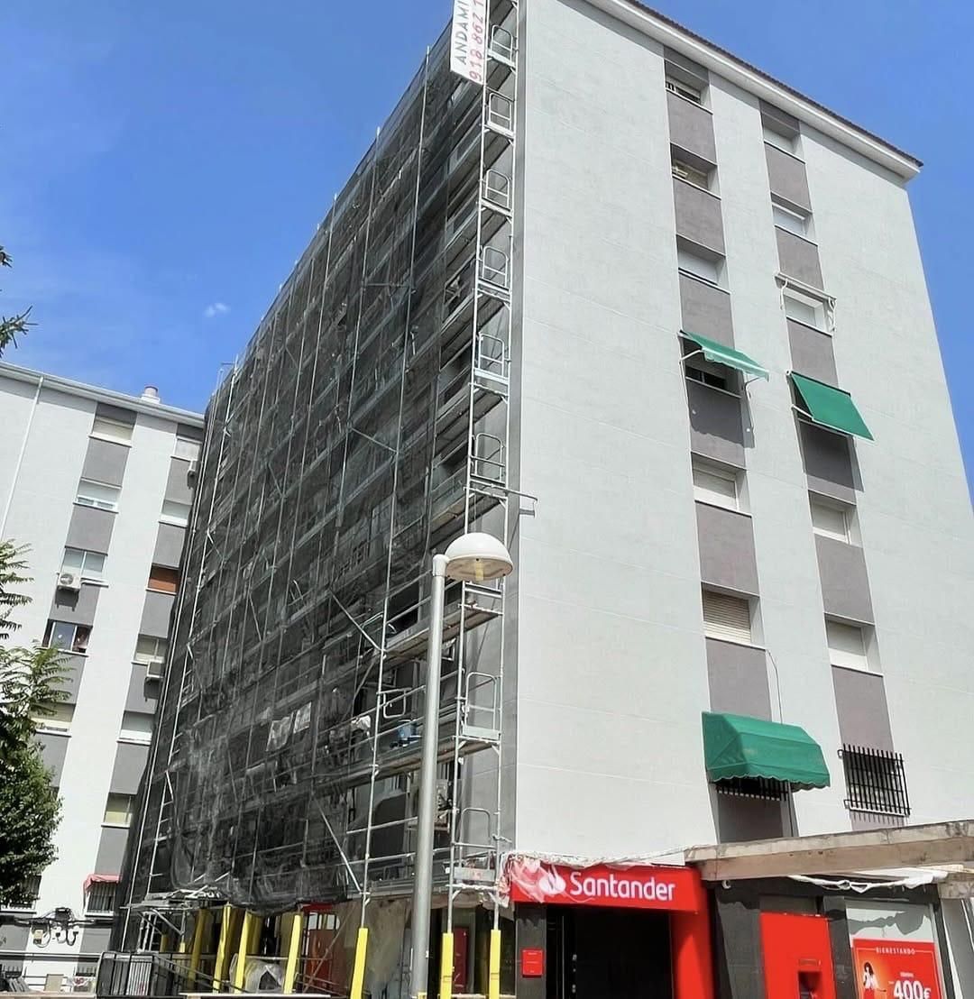 Edificio de apartamentos de varias plantas con andamios; letrero del banco Santander en la base.