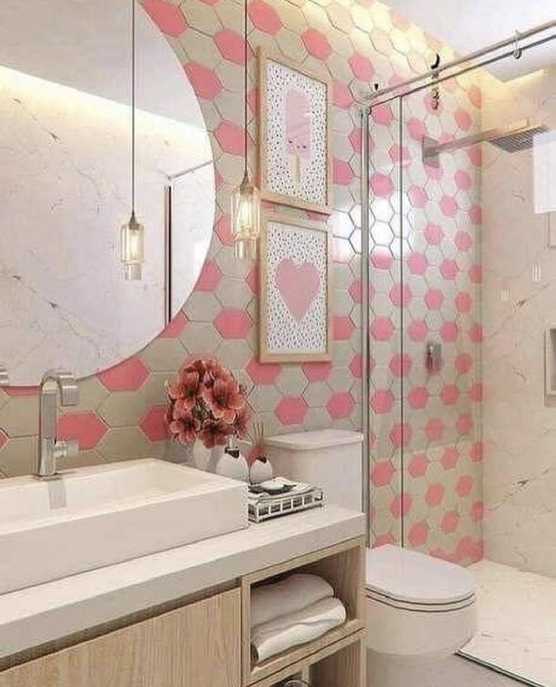 Baño rosa y gris con pared decorativa de azulejos hexagonales, lavabo blanco y cuadros enmarcados.