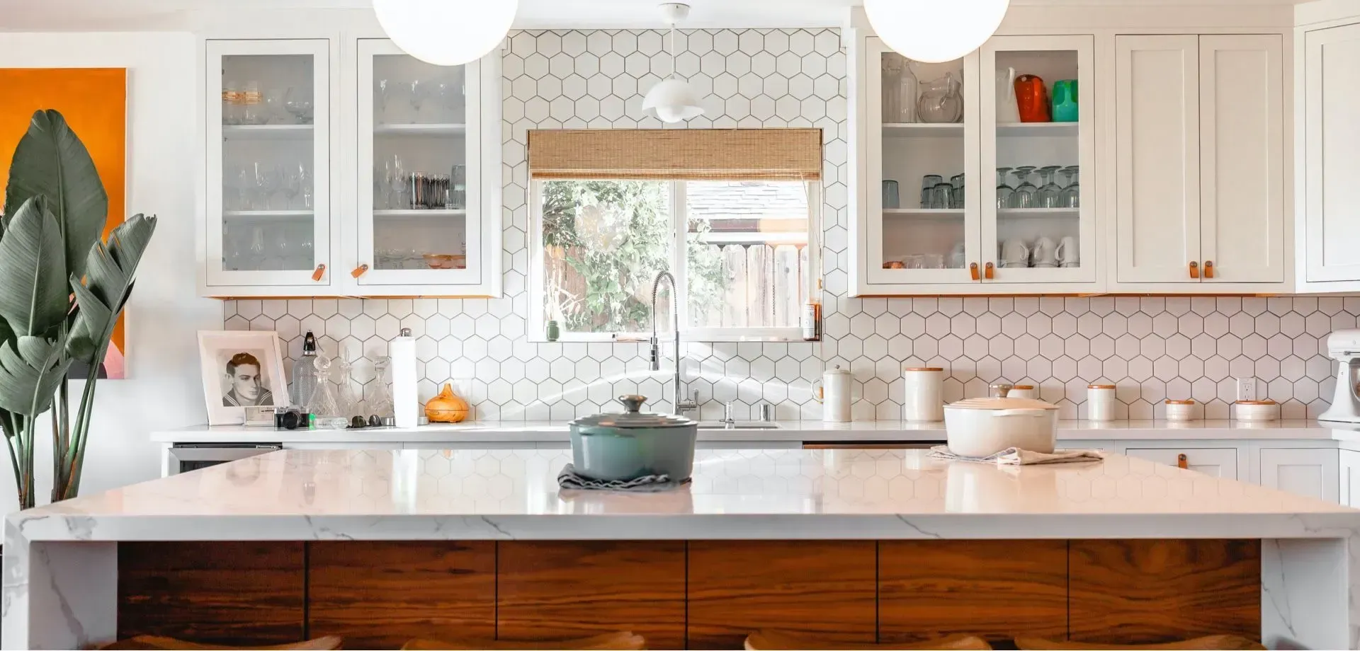 Interior de cocina con gabinetes blancos, encimera de mármol, isla de madera y salpicadero de azulejos hexagonales.