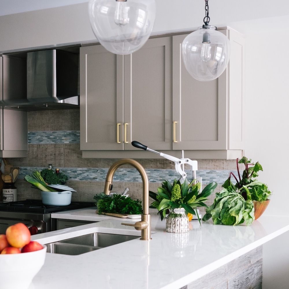 Cocina moderna con encimera blanca, grifo de latón, armarios grises y productos frescos.