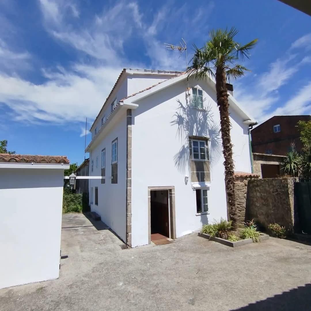 Edificio blanco con puerta abierta, palmera y cielo azul.