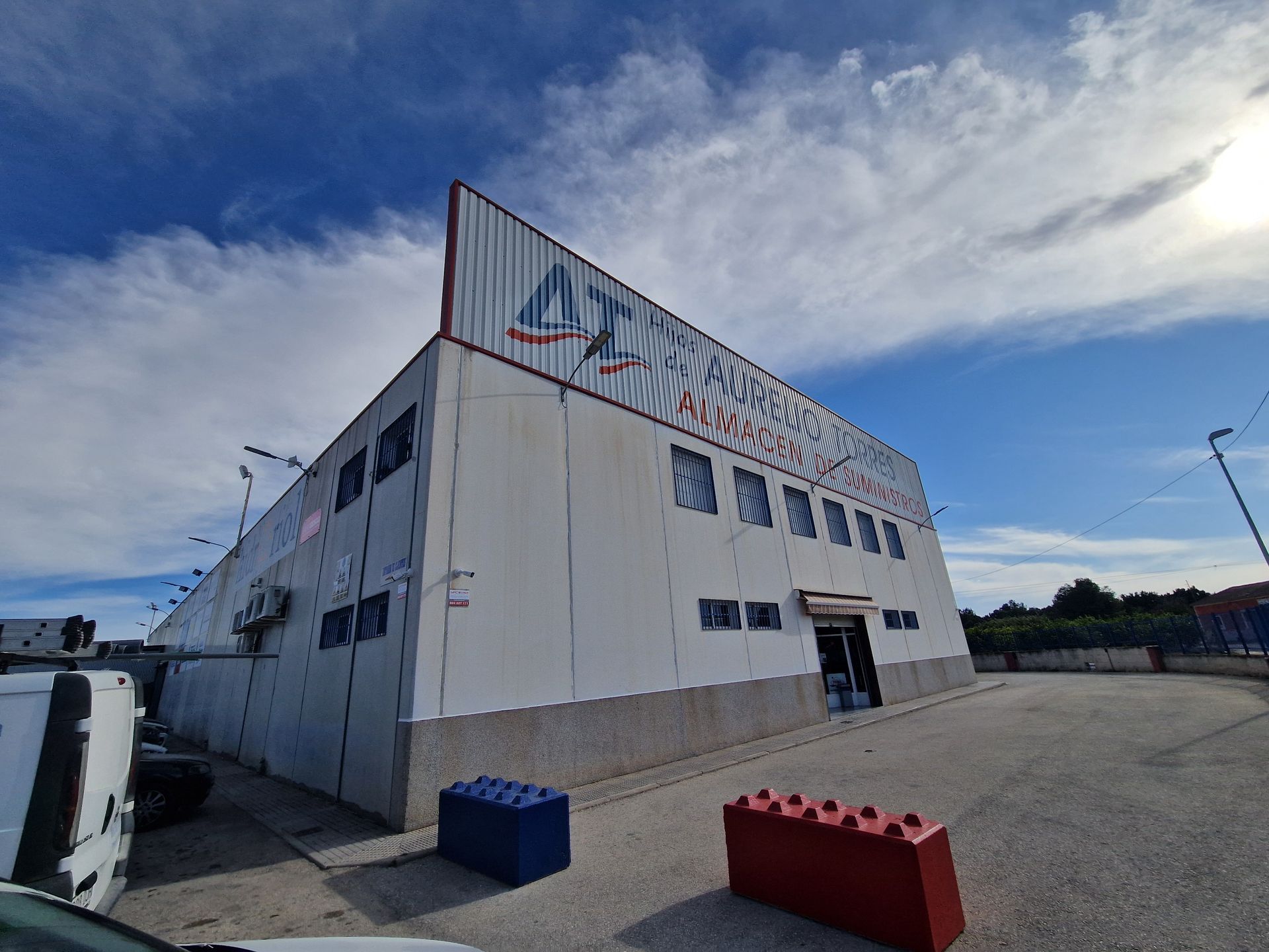Almacén con un gran letrero bajo un cielo azul. El edificio es blanco, con ventanas y una puerta marrón.