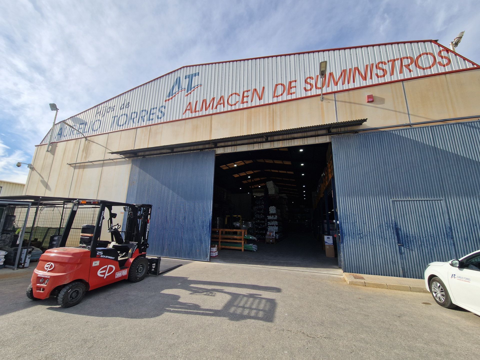 Entrada al almacén con puertas correderas abiertas, montacargas y señalización en español.