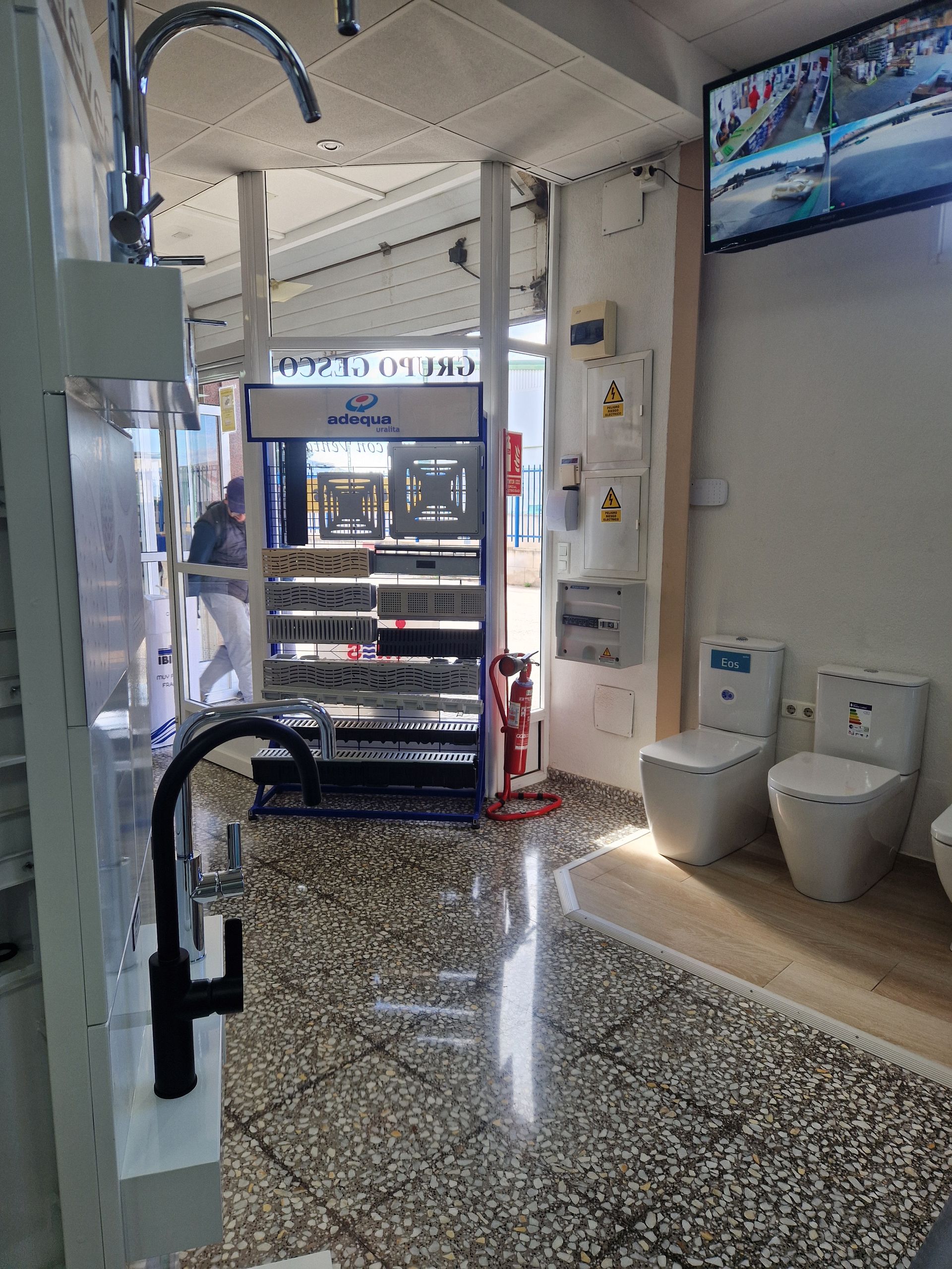 Interior de una tienda de artículos de plomería. Se ven grifos, inodoros y expositores; una persona camina por la entrada.